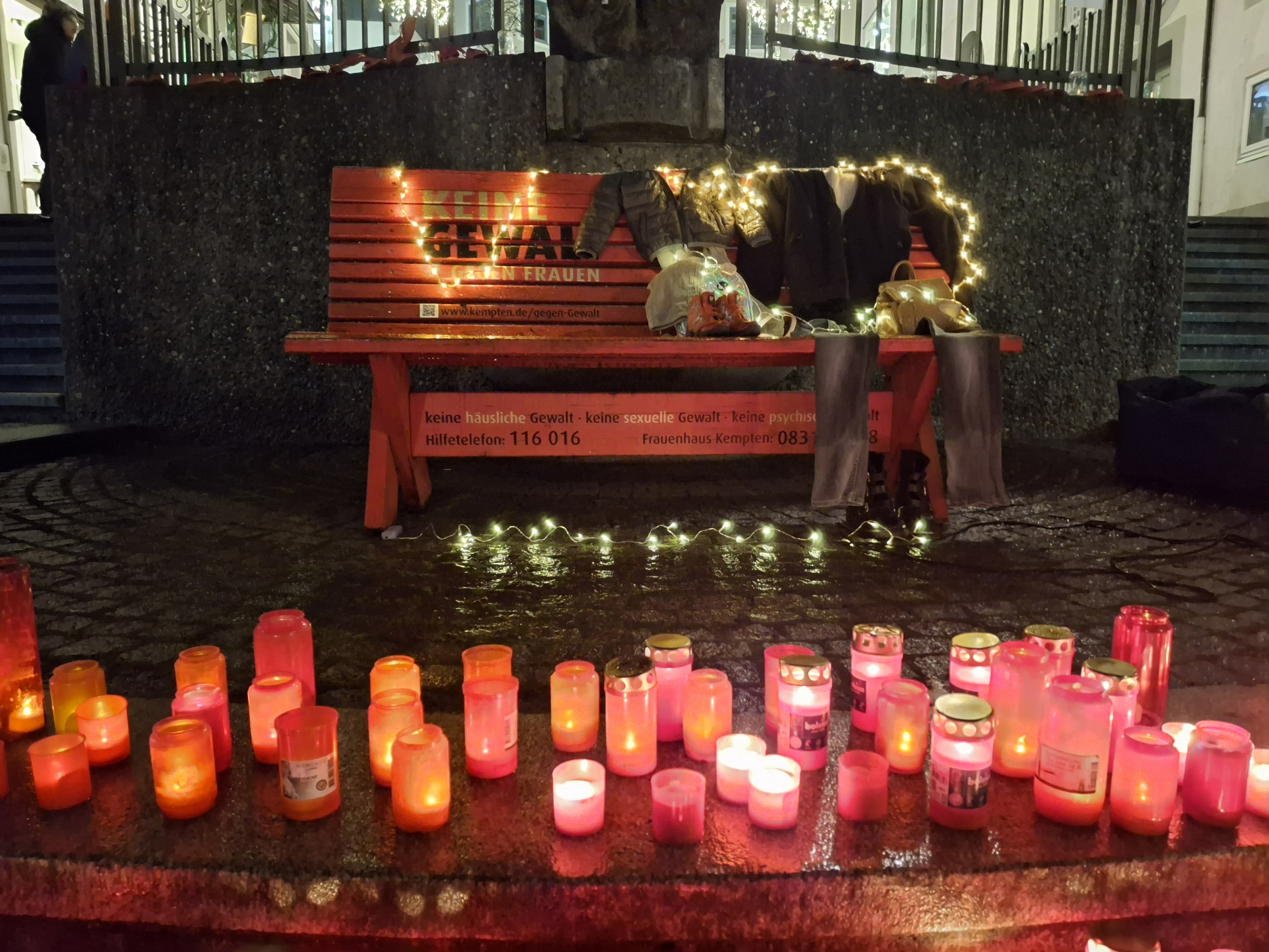 Die Rote Bank mit Kerzen, Lichtern und drapierten Kleidern von einem imaginären Paar.