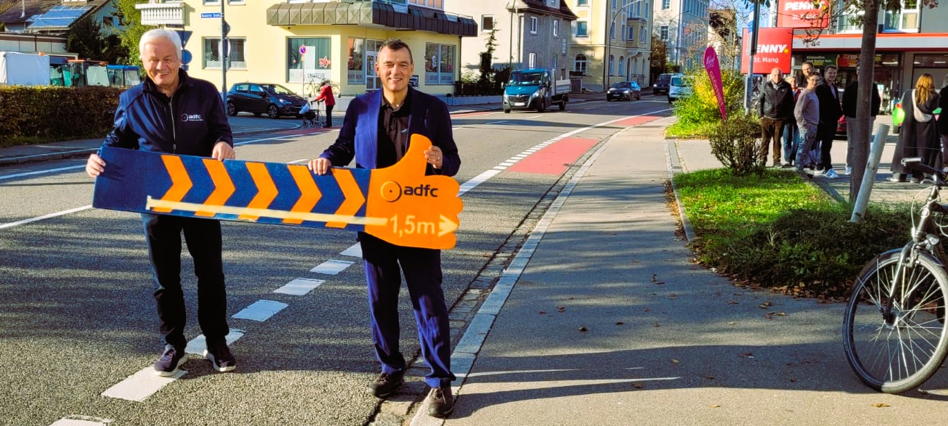 Lutz Bäucker und Thomas Zeh halten auf dem Fahrradstreifen ein öffentlichkeitswirksames Plakat zum Einhalten des Fahrabstands ins Bild.